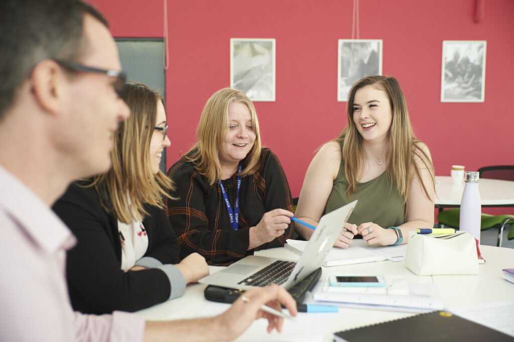 JTSCITT Trainees sat around a table chatting and laughing.