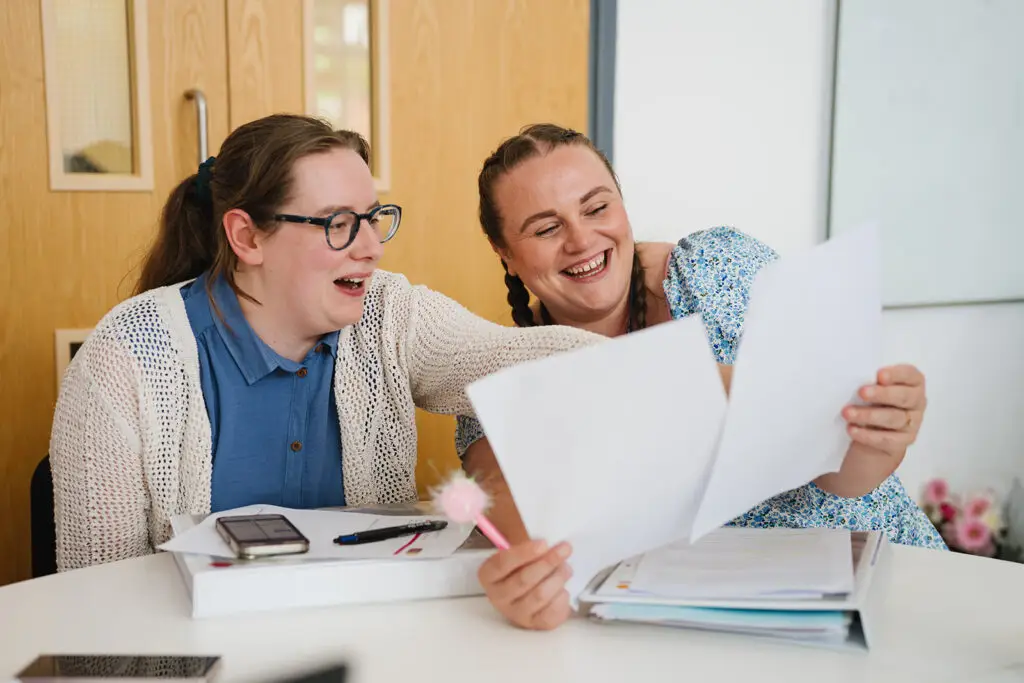 2 female JTSCITT trainees laughing together whilst looking at their work