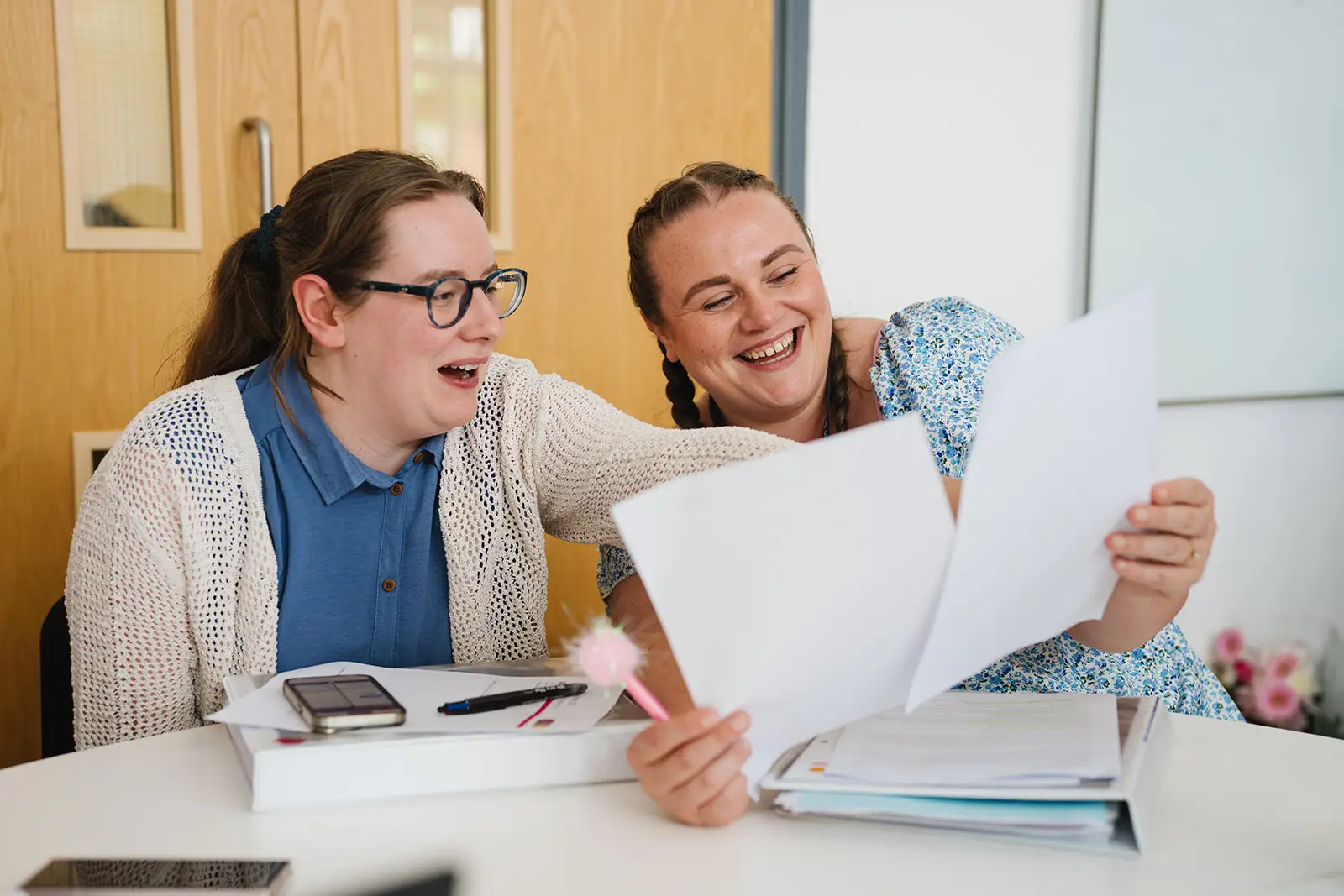 2 female JTSCITT trainees laughing together whilst looking at their work